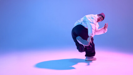 Street dancer performing dynamic pose in studio with colored light. Concept of sportswear advertising, fitness promotion, dance school branding and urban lifestyle visuals.