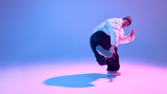 Street dancer performing dynamic pose in studio with colored light. Concept of sportswear advertising, fitness promotion, dance school branding and urban lifestyle visuals. - Powered by Adobe