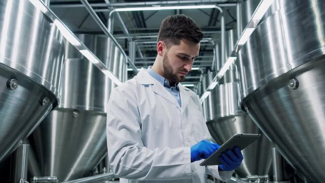 Male Food Factory Engineer Using Tablet to Monitor Dairy Production and Quality Control in Modern Beverage Plant