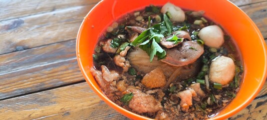 Pork noodle soup in an orange plate on a wooden table