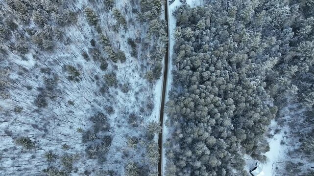 A top-down aerial shot over the Adirondack Mountains, showing a straight road bisecting a dense, snow-covered forest during a winter storm.