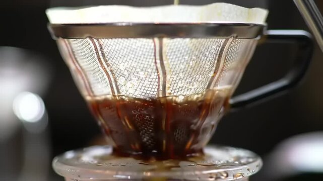 Close-up of a glass coffee dripper with a paper filter, brewing fresh coffee, showing the rich brown liquid dripping into a container below, with a shallow depth of field.