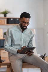 African American man working from home, holding a digital tablet and reviewing information in a modern home office, focused on online business, remote work, and professional productivity © lordn