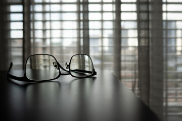 Eyeglasses on the table and light filtering through the curtains from the large window. Starting the day in the morning.