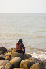 a woman wearing a hijab sits on the rocks on the beach