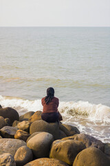 a woman wearing a hijab sits on the rocks on the beach