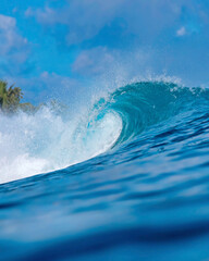 Massive blue ocean wave curling, bright turquoise barrel breaking with foamy crest and spray, sunlight