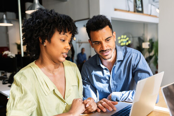 Multicultural coworkers discussing project on laptop in office. Professionals reviewing information together during a work session. Communication and teamwork concept.