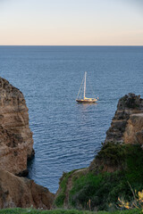 Catamaran sailing near the stunning Praia dos Pinheiros and picturesque Caves along the Algarve Coast in Portugal, on a bright sunny evening during sunset in Lagos, Portugal.