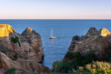 Catamaran sailing near the stunning Praia dos Pinheiros and picturesque Caves along the Algarve Coast in Portugal, on a bright sunny evening during sunset in Lagos, Portugal.