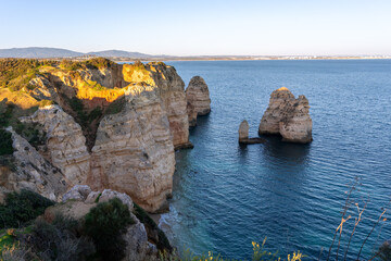 Jagged limestone cliffs rising dramatically from turquoise waters at Ponta da Piedade during sunset in Lagos, Portugal with vast Atlantic ocean in the background