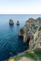 Jagged limestone cliffs rising dramatically from turquoise waters at Ponta da Piedade during sunset in Lagos, Portugal with vast Atlantic ocean in the background