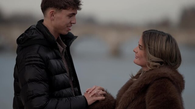 A young couple in Paris France holding hands with the river Seine and a bridge in the background The scene captures a moment of love and affection between the man and woman in a European setting.
