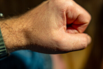 Close-up of a male hand forming a fist, symbolizing strength and determination. The textured skin and muscles are visible, emphasizing physicality and action. Suitable for motivational content.