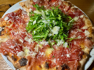 Rustic Wood Oven Pizza with Prosciutto, Arugula, and Parmesan Cheese on White Plate
