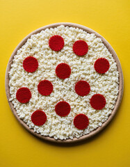 Creative pepperoni pizza made of felt, wool and craft material. This handmade food art with melted cheese and fuzzy texture playful concept on yellow background