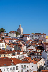 Obraz premium A telephoto view of the iconic white dome of the National Pantheon (Church of Santa Engracia) rising above the dense, colorful architecture and orange terracotta roofs of the Alfama neighborhood.