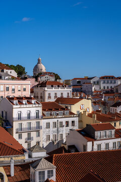 High-angle view from Miradouro do Recolhimento showing the red-tiled rooftops of Lisbon, the Church of Santo Estevao, the National Pantheon dome, and the Tagus River under a clear blue sky.