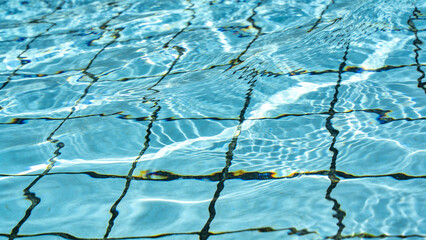 Clear blue water in a swimming pool with tiled floor visible beneath the surface