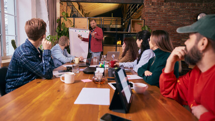 Business team listening to presentation in modern coworking space. Concept of leadership communication, shared goals, professional growth and collaborative office environment.