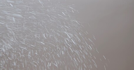 White particles or snowflakes falling diagonally on a soft purple background with a motion blur effect.