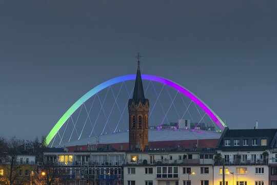 Evening view of residential buildings on the banks of the Rhine, behind them the church tower of St. John's Church and the rainbow illuminated arch of the Lanxess Arena, Cologne-Deutz, Cologne, North Rhine-Westphalia, Germany