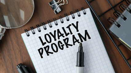 LOYALTY PROGRAM - words on a yellow notebook on a background of digital tables, a magnifying glass and marker