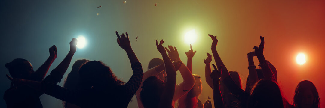 Silhouettes of dancing people beneath bright stage lights. Concept of New Year concert mood, shared emotions, nightlife culture, youth energy and modern event branding visuals. Banner