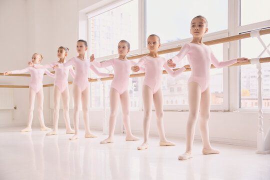 Line of young ballet dancers practicing balance at studio barre. Concept of physical stability training, body control education, balance improvement exercises, early dance development. - Powered by Adobe