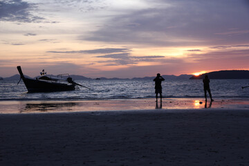 People silhouetted while taking pictures of the colourful sunset over the Andaman Sea from Railay Beach, Krabi, Thailand