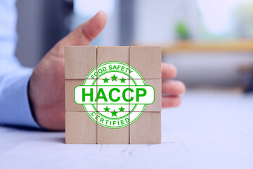 Food safety HACCP certified concept with hand push on wooden cube to approve the hazard analysis and critical control point with certificate represent to quality control in food factory industries