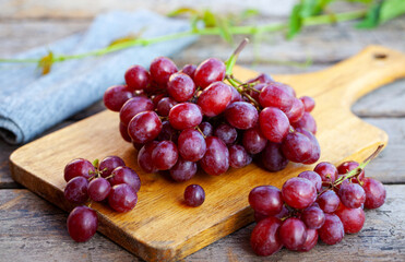 Fresh red grapes cluster on cutting board. Rustic wooden background. Close up.