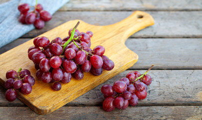 Fresh red grapes cluster on cutting board. Rustic wooden background. Close up. Copy space. © annapustynnikova