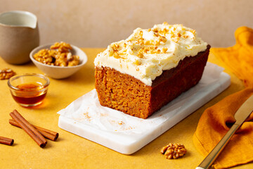 Carrot cake loaf on a white marble serving board. Yellow background. Close up.