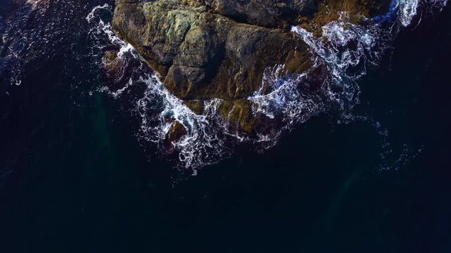 Water crashes against strong stone formations, sending sprays of foam into the cool evening air as the tide ebbs and flows with rhythmic grace at the tranquil coastline.