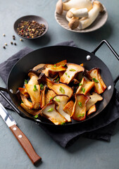 Roasted king oyster mushrooms in skillet, garnished with green onions. Grey background.