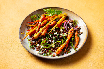 Warm salad. Roasted carrots with lentil, arugula and feta cheese. Yellow background. Close up.