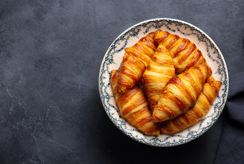 Fresh croissants on decorative plate, French pastry elegance, breakfast indulgence. Grey background. Copy space. Top view.
