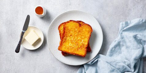 French toast on white plate, with butter and maple syrup. Grey background. Top view.