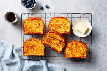 Golden French toast slices cooling on rack, served with butter, blueberries and maple syrup. Top view.