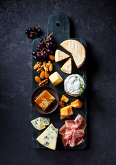Assortment of cheese with jamon, fresh grape and nuts on marble cutting board. Dark background. Top view.