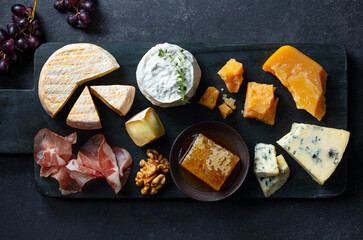 Assortment of cheese with jamon, fresh grape and nuts on marble cutting board. Dark background. Top view.