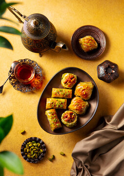 Baklava dessert on a stand served with tea in armudu glass from a copper teapot. Warm yellow background. Top view.