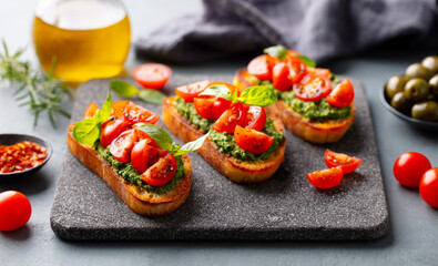 Tomato, pesto bruschetta, crostini with fresh basil on stone serving board. Grey background. Close up.