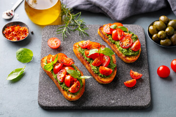 Tomato, pesto bruschetta, crostini with fresh basil on stone serving board. Grey background. Close up.