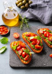 Tomato, pesto bruschetta, crostini with fresh basil on stone serving board. Grey background.