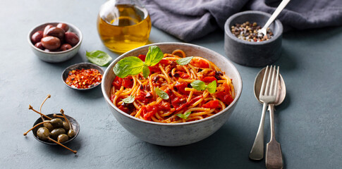 Italian spaghetti pomodoro with basil, olive oil, olives, pepper blend, rustic styling. Grey background. Close up.