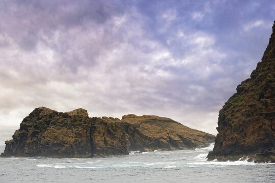 Rocky island 'Iieu Deitado' under a dramatic cloudy sky with gentle waves at the base, Iieu Deitado, Iieu em Pe, Horta, Faial, Azores, Portugal