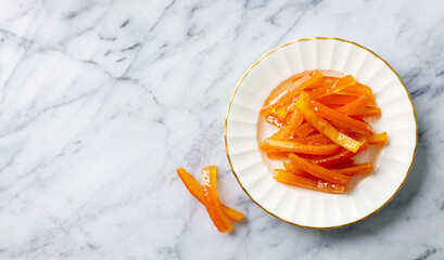 Candied orange peels on elegant plate. Marble background. Copy space. Top view.