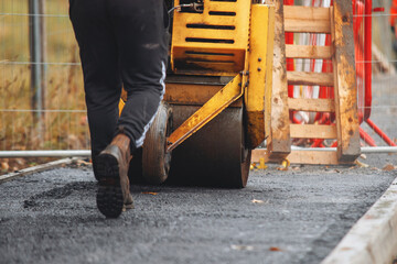 Construction worker operating road roller on freshly paved hot asphalt surface